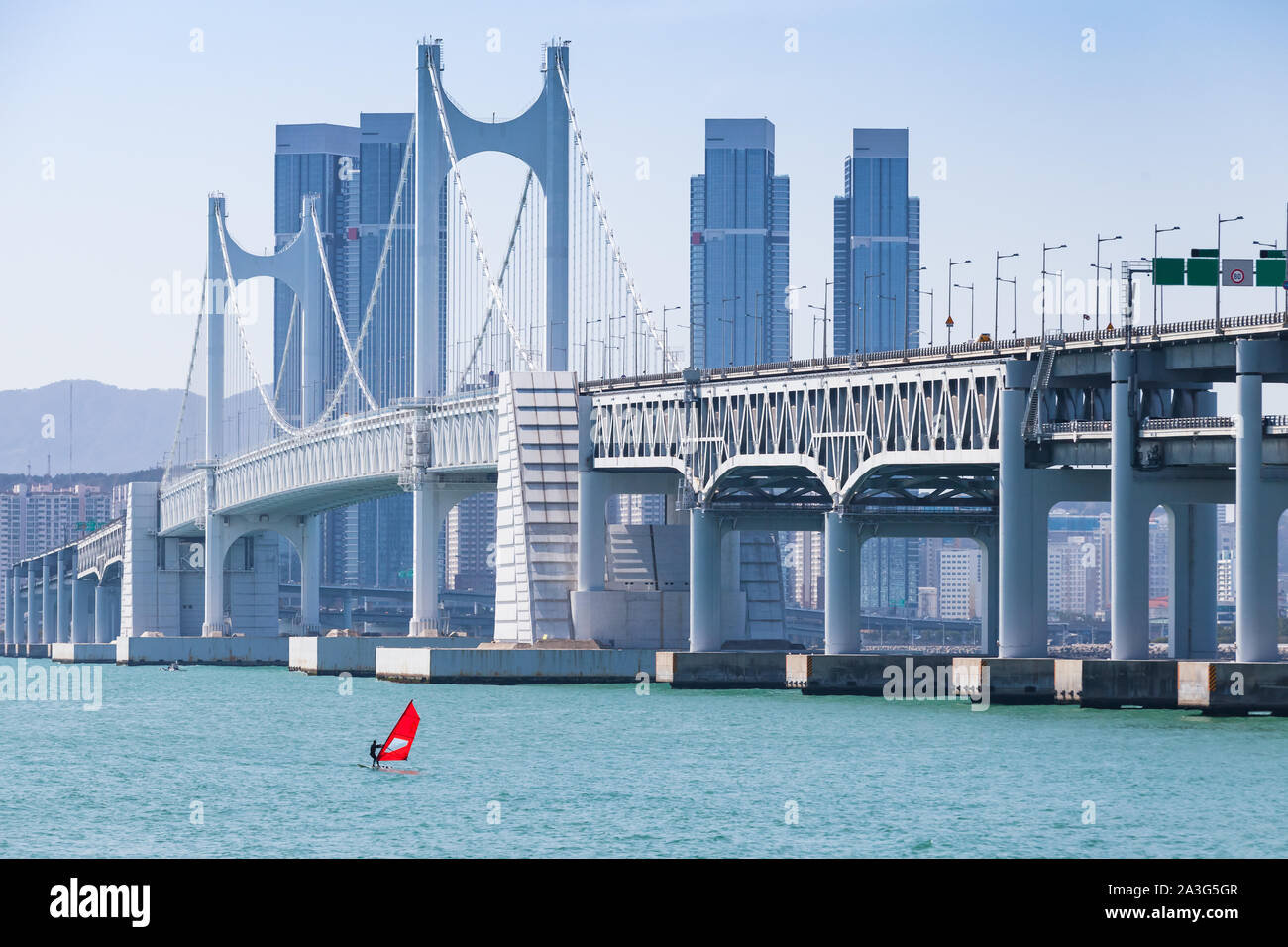 Stadtbild mit Gwangandaegyo oder Diamond Bridge. Windsurfer mit roten Segeln geht in der Nähe der Hängebrücke in Busan, Südkorea Stockfoto