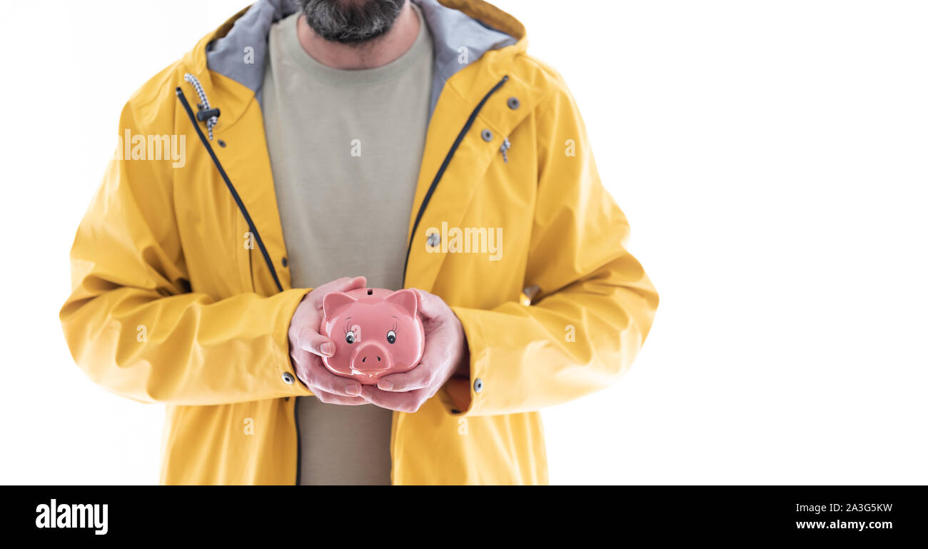 Mittelteil der Mann im gelben Regenmantel Holding rosa Sparschwein in beiden Händen Stockfoto
