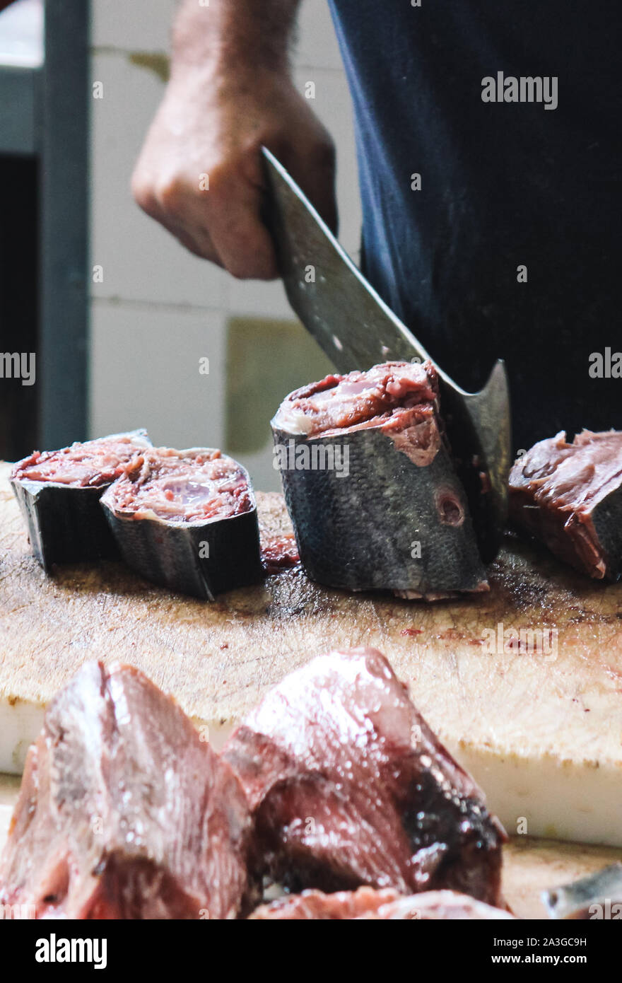 Detail von einem Fischer schneidet Thunfisch mit einem riesigen Cleaver auf einem Holzbrett. Verschwommen Thunfisch, Fleisch in den Vordergrund. Traditionellen Fischmarkt in Funchal, Madeira, Portugal. Fischerei, Fischerei. Stockfoto