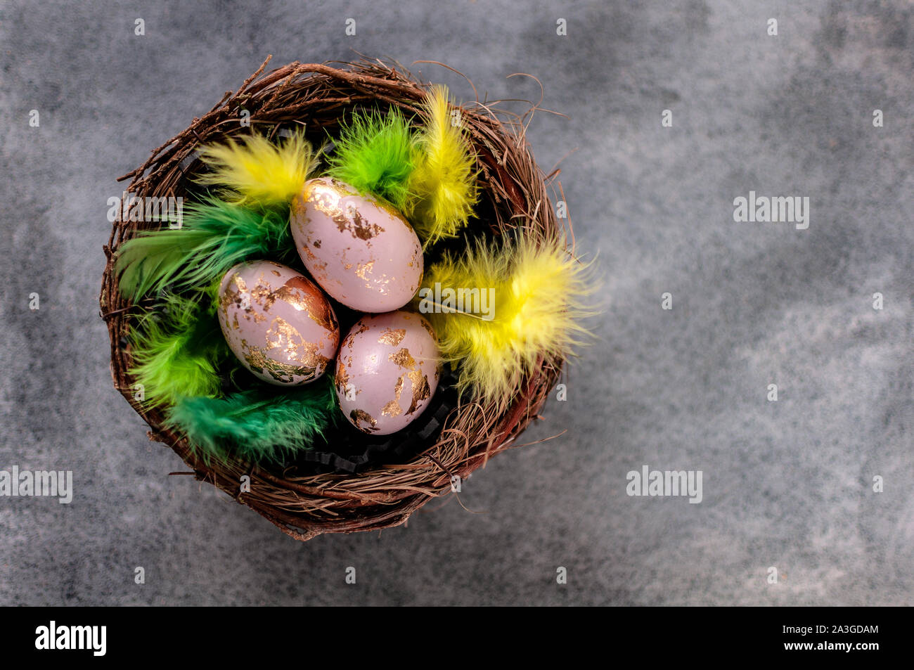 Ostereier, bemalt und gold verspiegelt, in einem Nest mit grünen und gelben Federn. Schöne traditionelle Ostern Dekoration auf einer grundge Granit oder Beton backgro Stockfoto