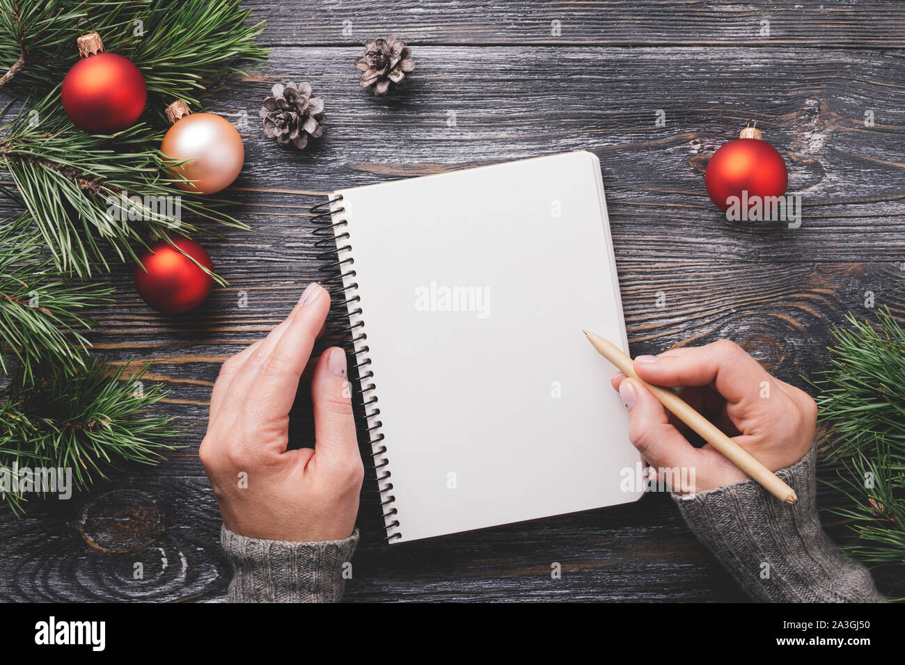 Woman's Hand writting in Notizbuch aus Papier. Weihnachten Dekorationen auf Holztisch, Ansicht von oben. Stockfoto