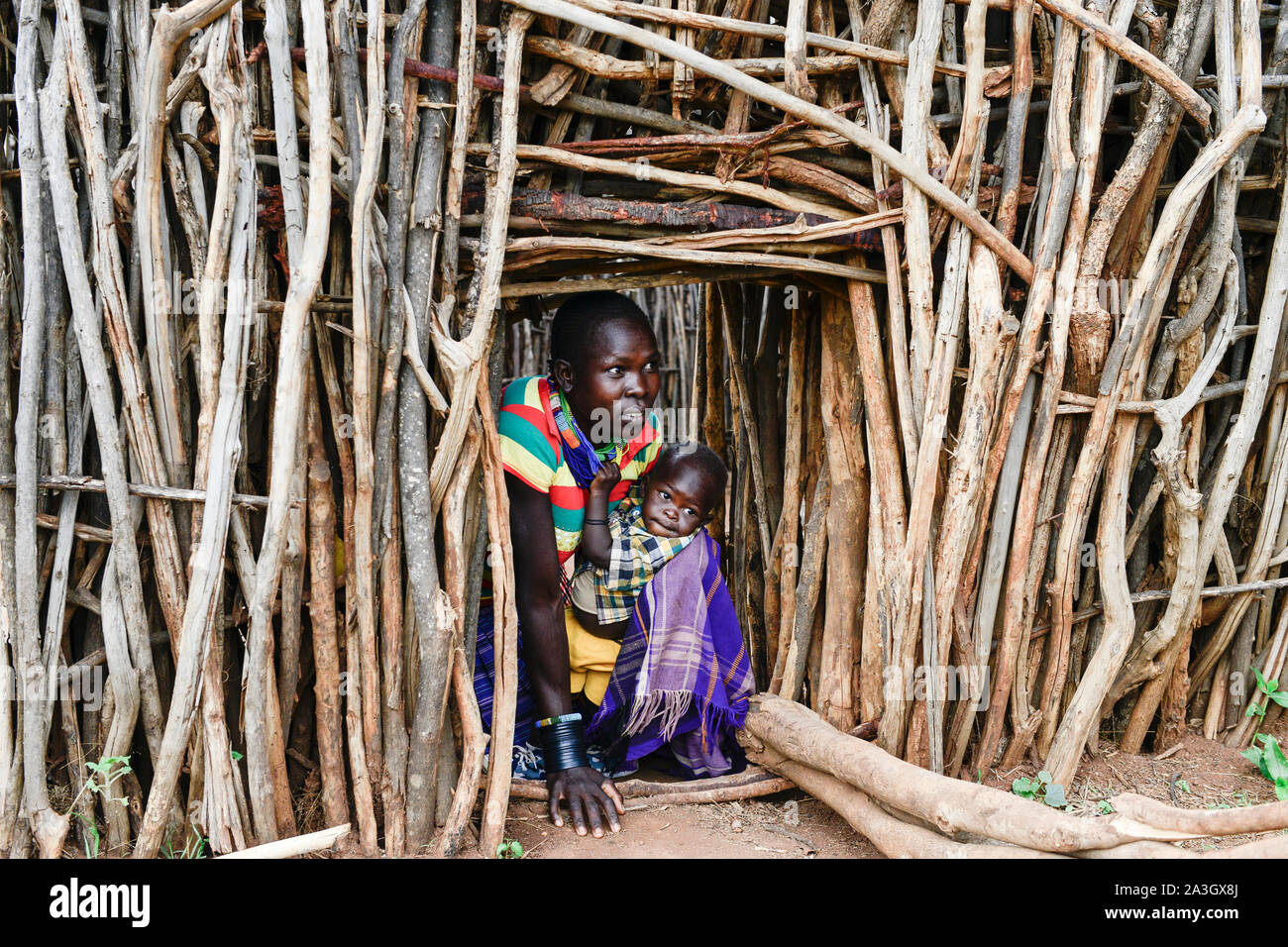 UGANDA, Karamoja, Kaabong, Lochom Karamojong Stamm, Dorf, Frau mit ihrem Baby am Eingang des Sticks eingezäunt Dorf die Startseite von feindlichen Stämmen und Vieh Raider zu schützen. Stockfoto
