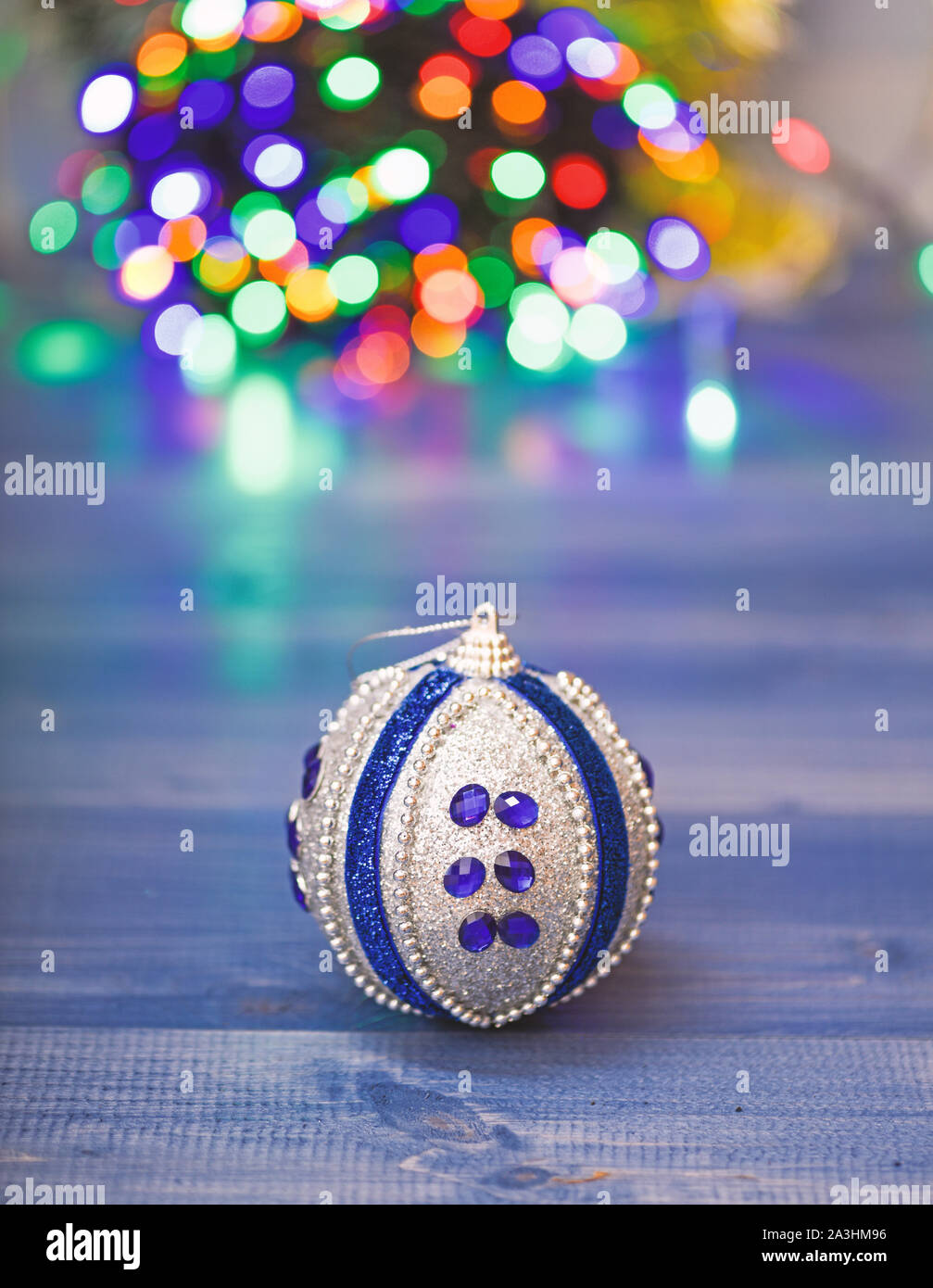 Weihnachtsbaumschmuck Konzept. Ball Ornament auf Blau Holz- Oberfläche. Farbenfrohe Einrichtung für den Weihnachtsbaum holen. Christmas ornament Single Ball am defokussierten Girlande bunte Lichter Hintergrund. Stockfoto