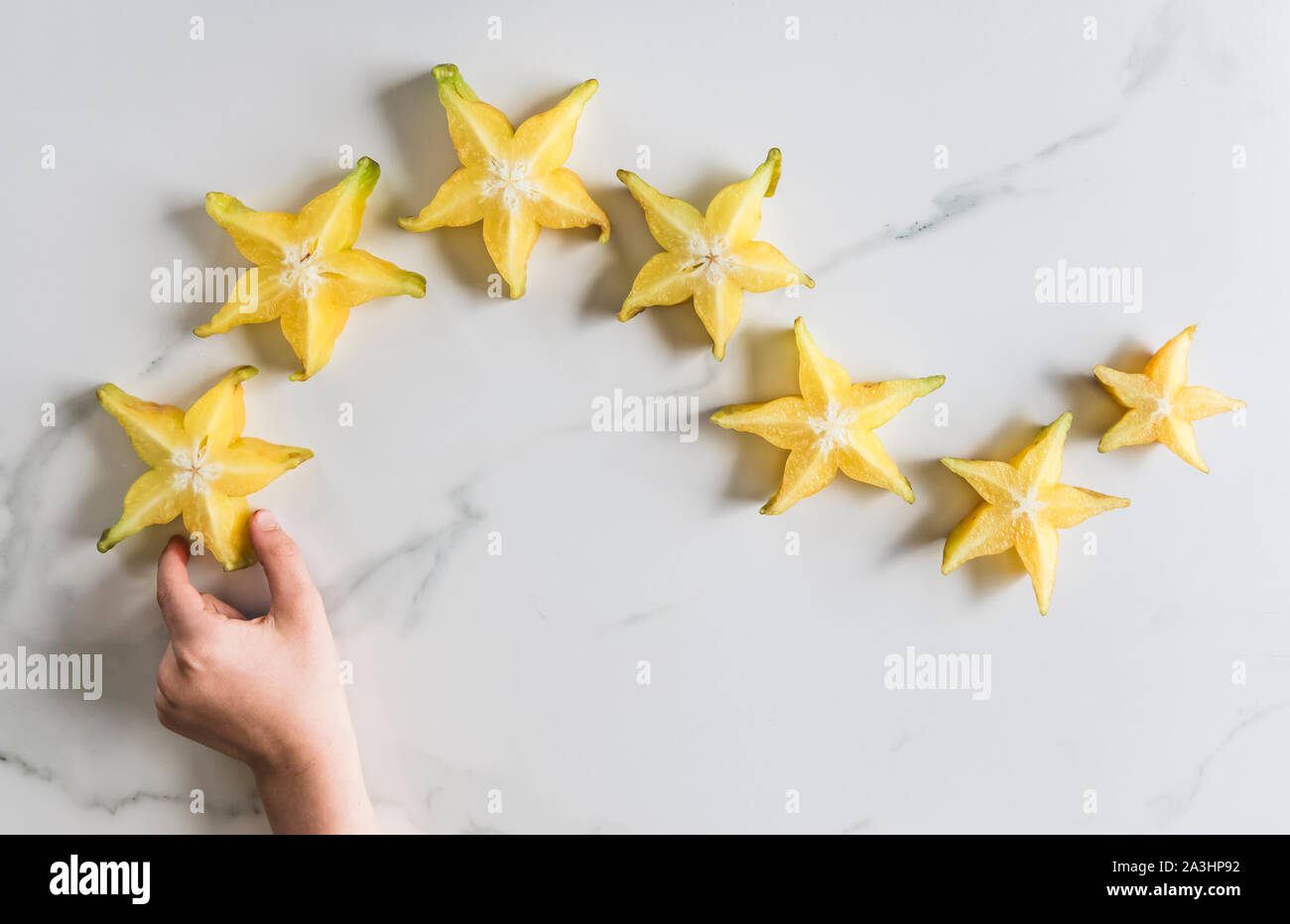 Hand erreichen für frisch geschnittene Scheibe Star Fruit auf weißem Marmor. Stockfoto