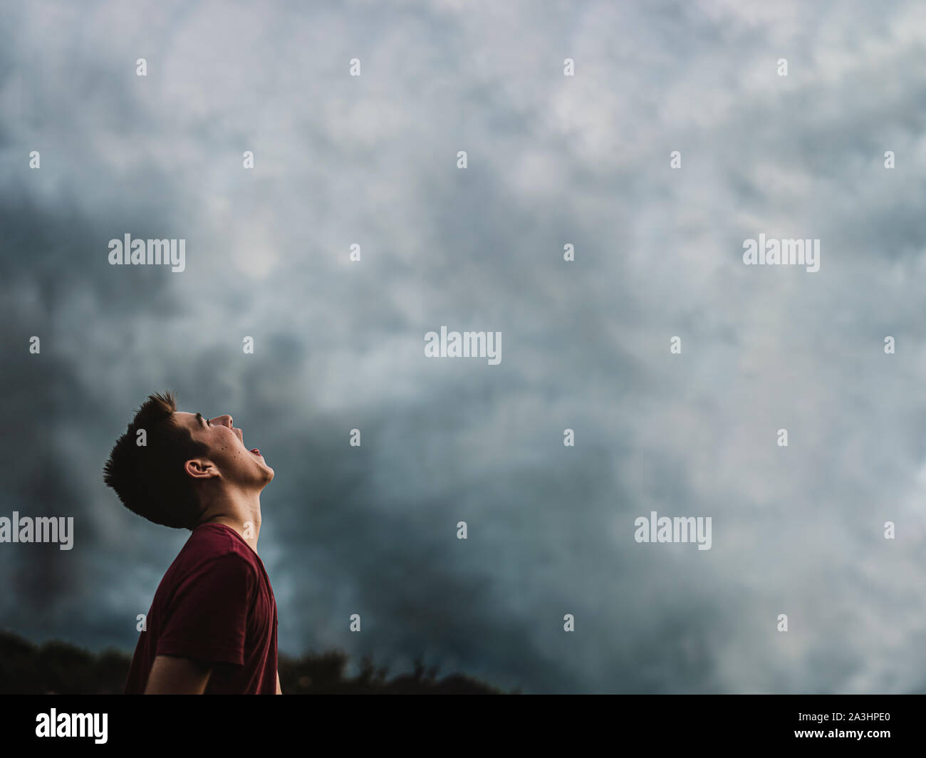 Jugendlich Junge zu dunklen bewölkten Himmel mit seinen Mund weit öffnen. Stockfoto