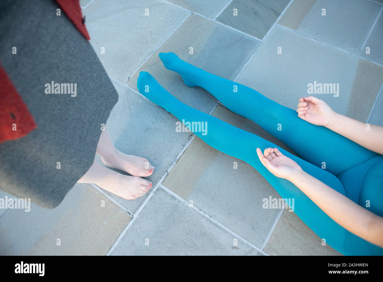 Hohe Betrachtungswinkel von zwei Frauen, eine in Blau Gymnastikanzug sitzen auf dem Boden Mit Beine verlängert, während das andere steht in der Nähe im Kleid und Netz Strümpfe, Vie Stockfoto