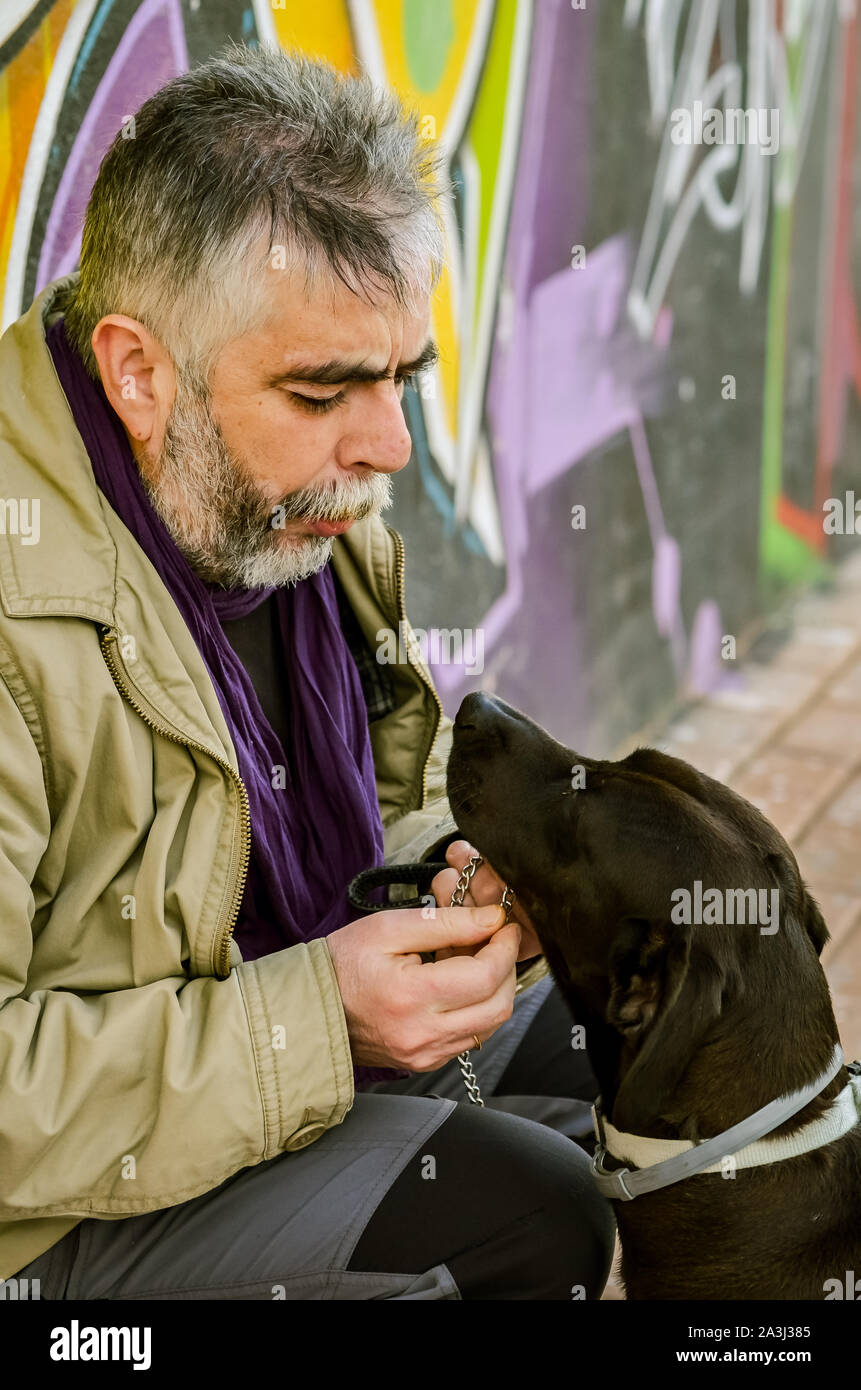 Reifer Mann mit Bart sieht Gesicht an einem schwarzen Hund zu Gesicht Stockfoto