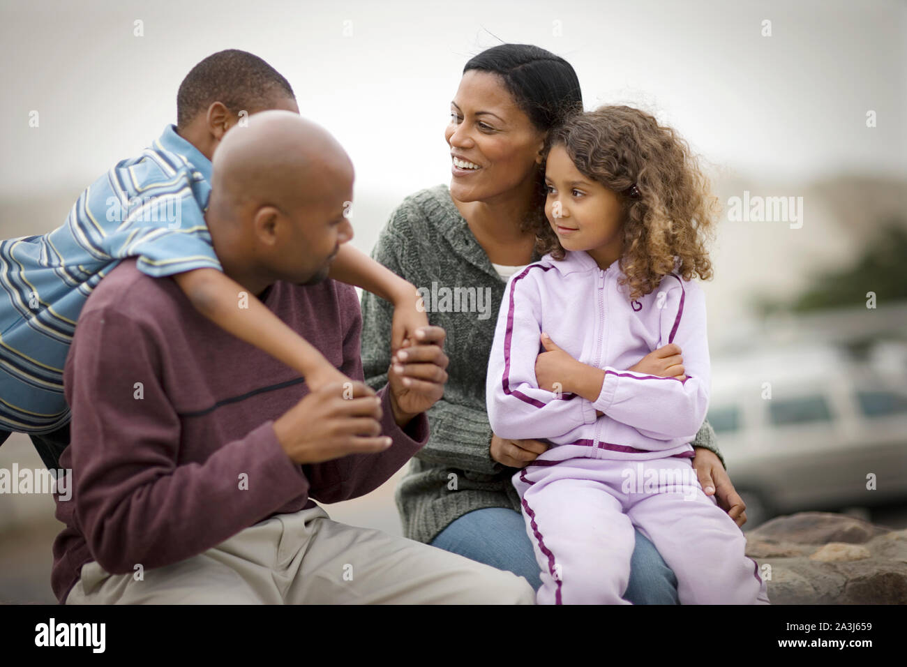 Gerne Mitte - erwachsene Paare und ihre zwei kleinen Kinder sitzen auf einer Mauer aus Stein im Freien. Stockfoto