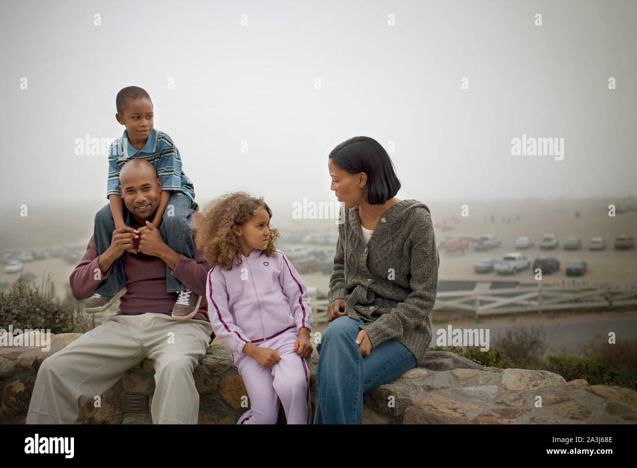 Gerne Mitte - erwachsene Paare und ihre zwei kleinen Kinder sitzen auf einer Mauer aus Stein im Freien. Stockfoto