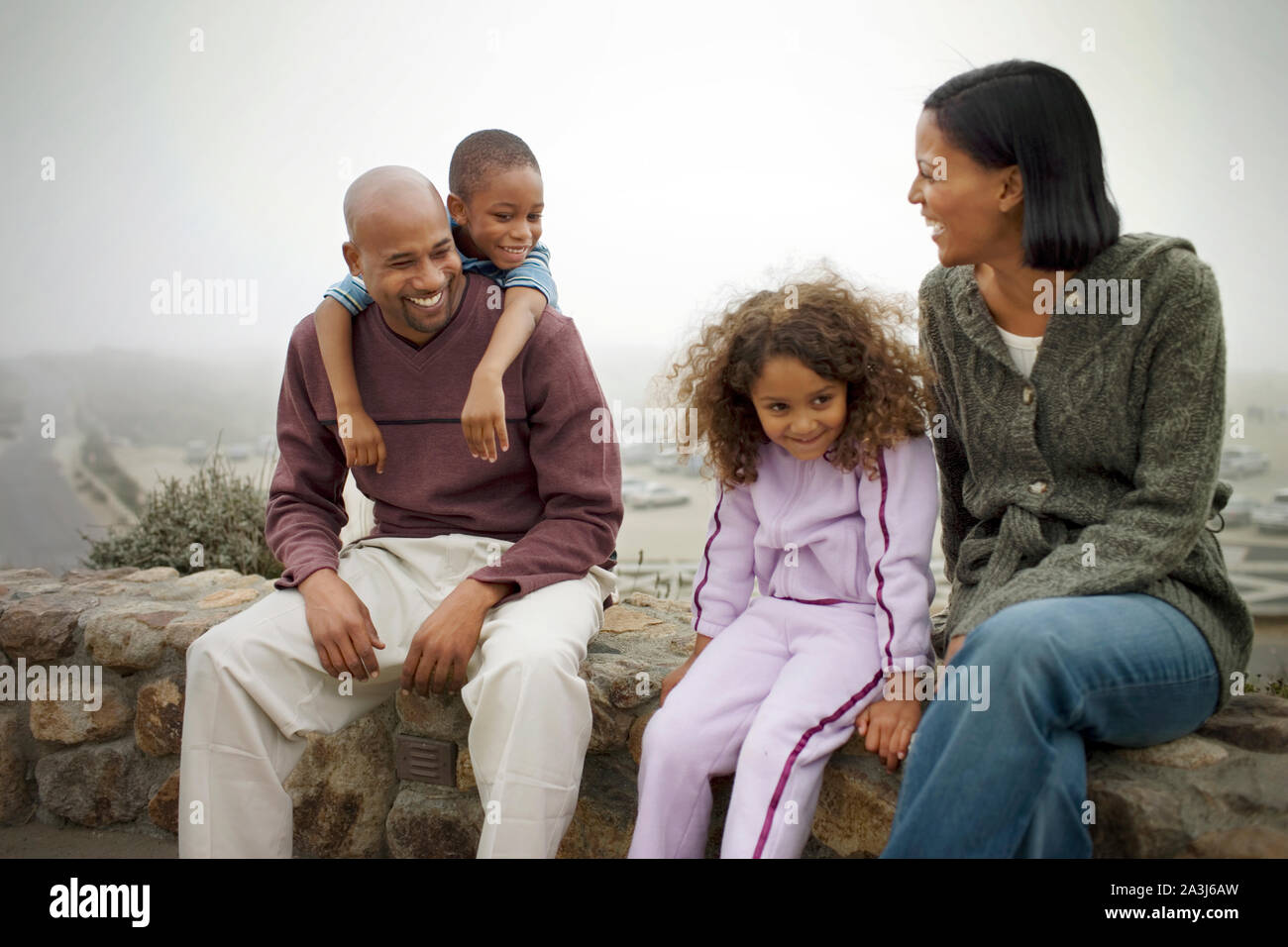 Gerne Mitte - erwachsene Paare und ihre zwei kleinen Kinder sitzen auf einer Mauer aus Stein im Freien. Stockfoto