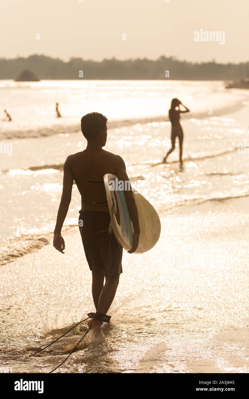 Man Walking am tropischen Strand von Midigama, Sri Lanka an sunsen 4 mit Surfbrett in der Hand. Stockfoto