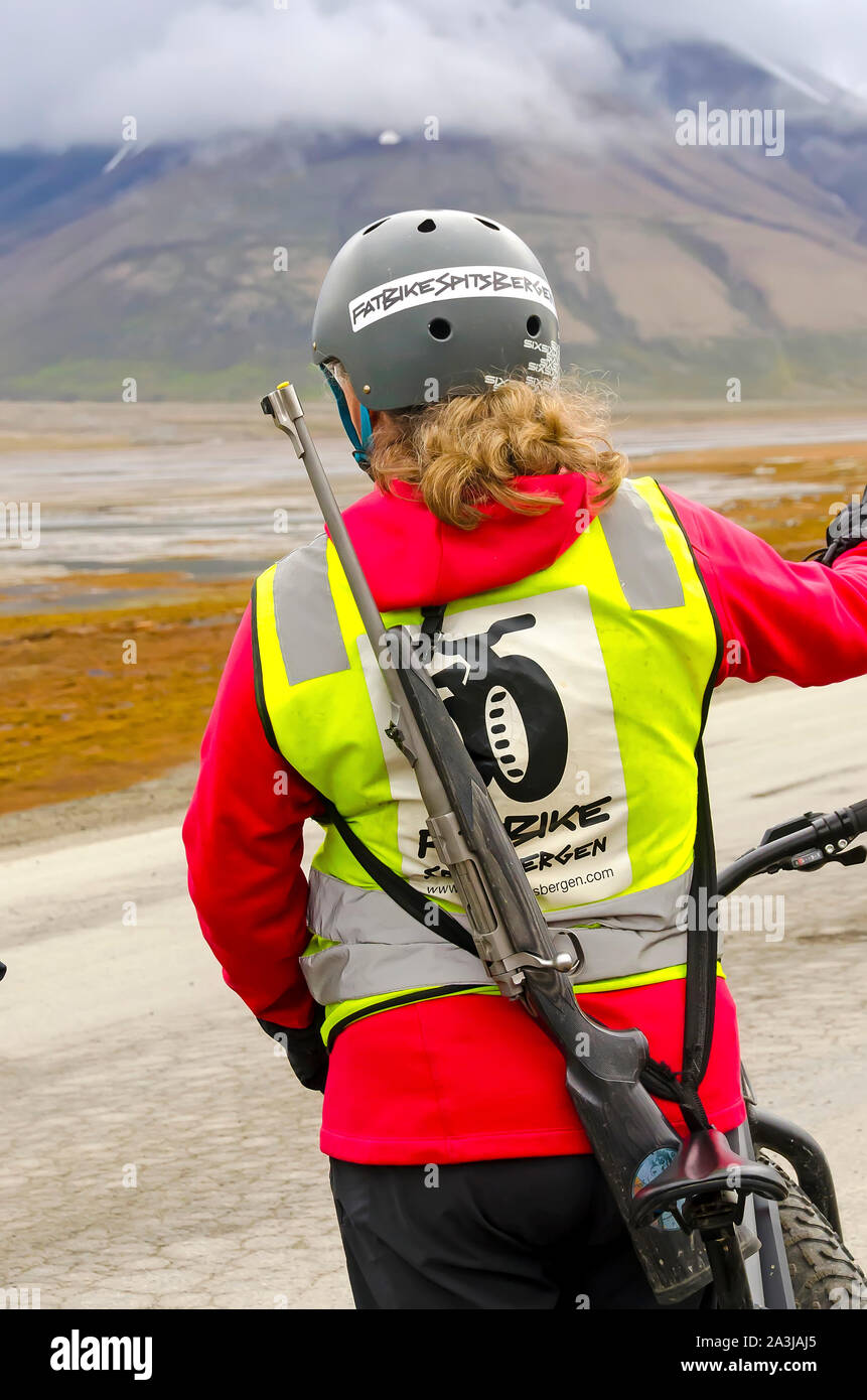 Frau auf Fahrrad trägt Eisbär Gewehr, Longyearbyen, Svalbard, Norwegen Stockfoto