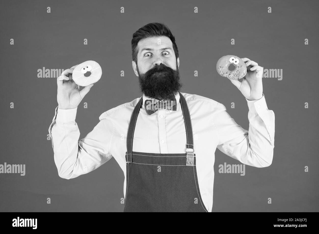 Catering Bäckerei Produkte an Sie. Der bärtige Mann mit Ring Donuts in der Bäckerei. Professionelle Bäcker mit glasierten Bäckerei Essen auf roten Hintergrund. Die perfekte Donuts aus unserer Bäckerei. Stockfoto