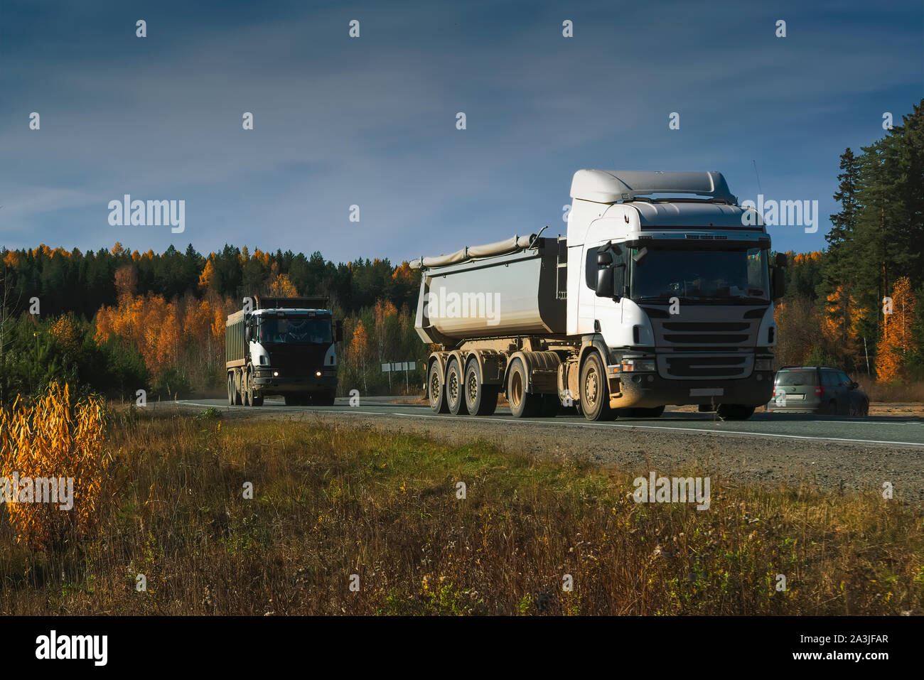 Weiße Lkw fahren auf der Asphaltstrasse in ländlichen Landschaft bei Sonnenuntergang. Stockfoto