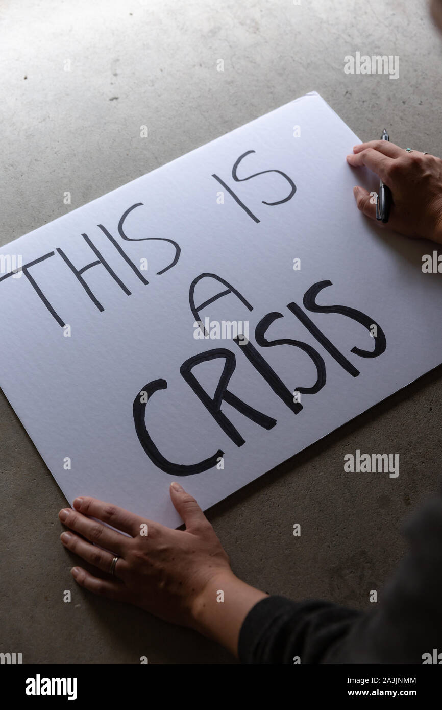 Anonym weiblich, Protest Zeichen, das sagt Dies ist eine Krise. Stockfoto