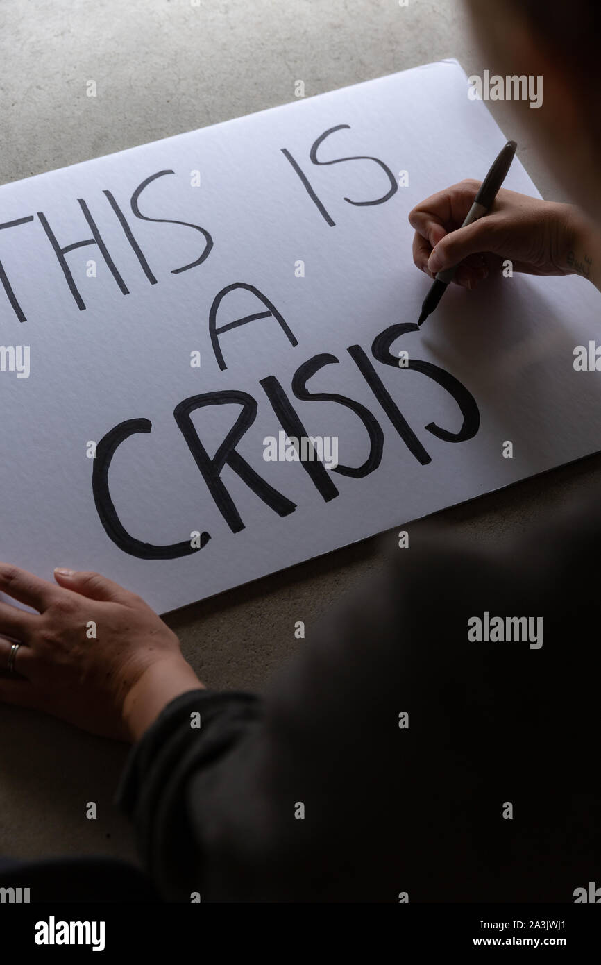 Anonym weiblich, Protest Zeichen, das sagt Dies ist eine Krise. Stockfoto