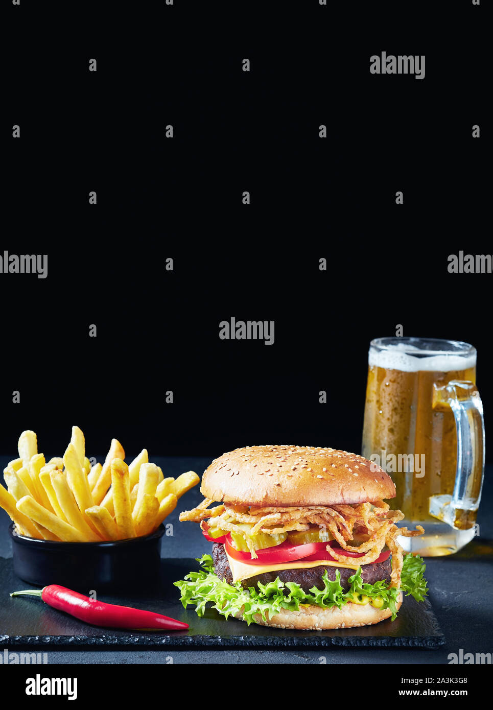 In der Nähe von Cheeseburger mit Cheddar Käse, knusprig gebratenen Zwiebeln, Salat, Tomaten, Gurken, Pommes und Bier im Glas mug Am bla Stockfoto