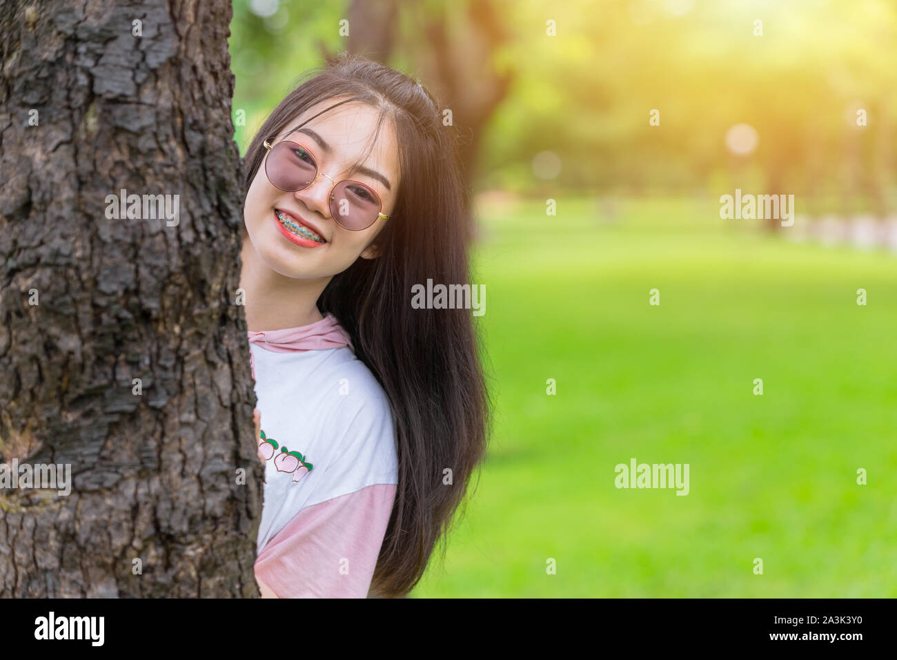 Gerne asiatische Zahnspangen Mädchen tragen Sonnenbrillen gerne Verstecken, Tree Park Outdoor Portrait suchen. Stockfoto