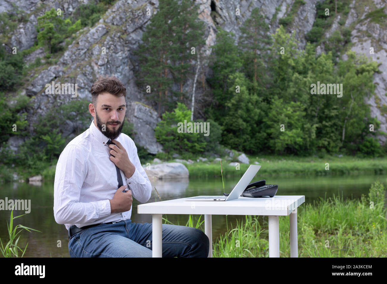 Bärtiger junger Mann mit Laptop outdoor. Geschäftsmann funktioniert immer, selbst wenn im Urlaub Stockfoto