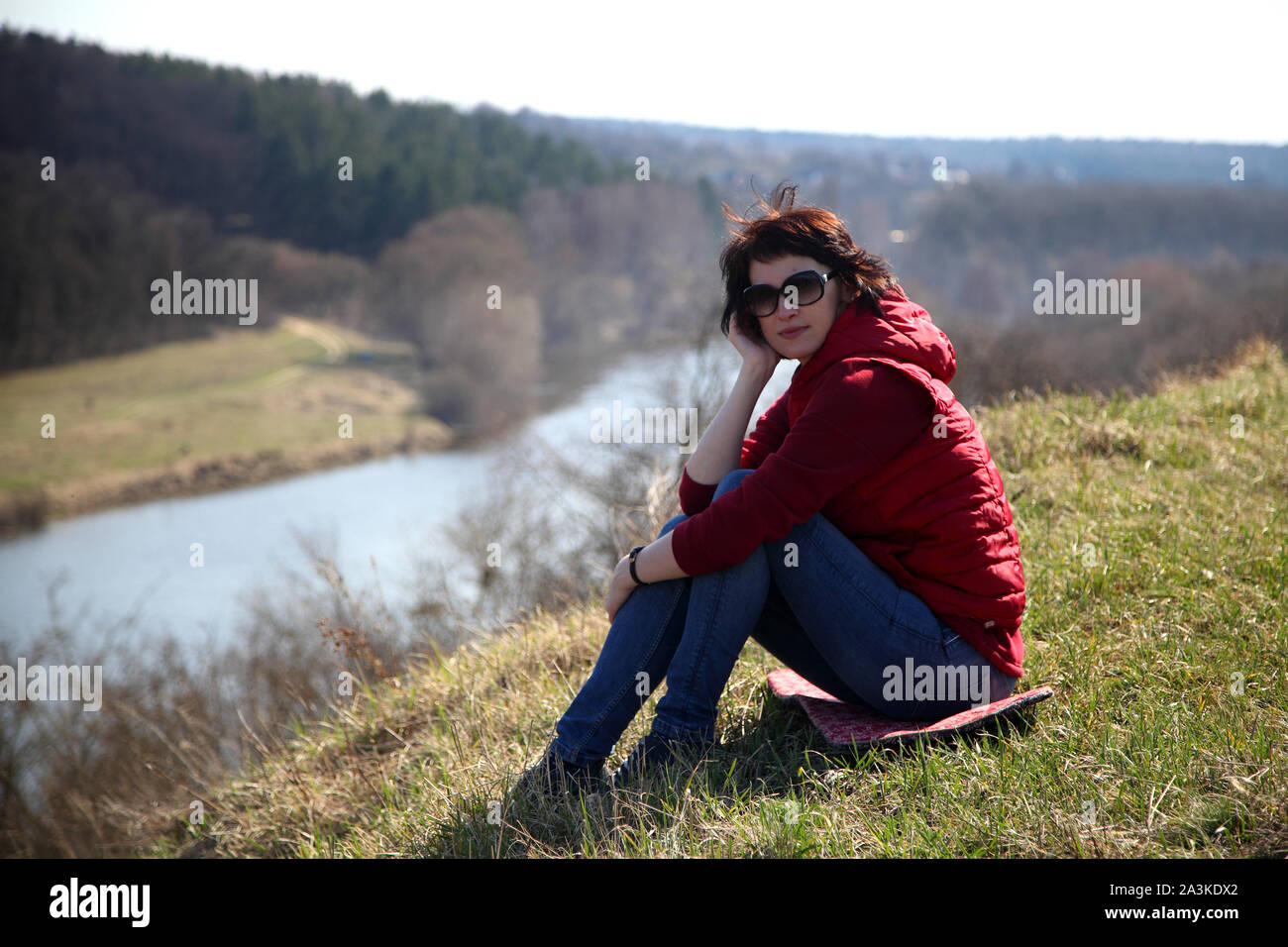 Ein Mädchen sammelt Schneeglöckchen im Wald. Schöne junge Frau taucht in den Strahlen der Frühlingssonne auf einer Lichtung im Wald. Stockfoto