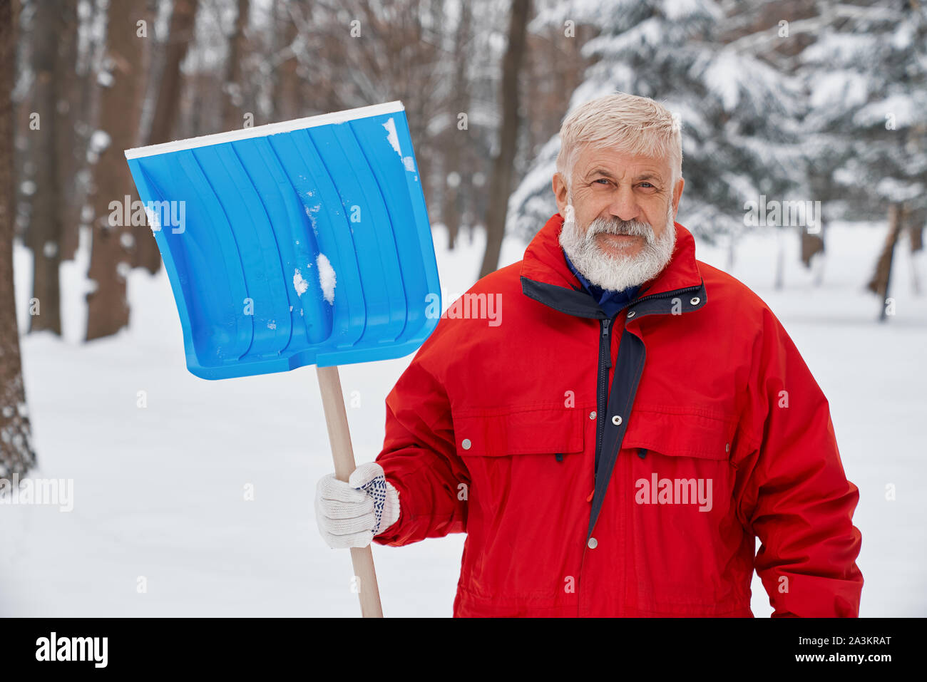 Vorderansicht der älteren Mann in Uniform, Schaufel und Suchen an der Kamera, während Schnee Reinigung von Straßen. Männliche Hausmeister posiert während der Morgen im Winter arbeiten. Konzept der Wartung. Stockfoto