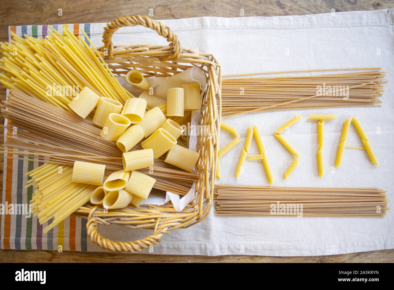 Pasta Wort mit Stücken von pennette Pasta in der Nähe von einem hölzernen Warenkorb der sortierten Auswahl an Pasta geschrieben Stockfoto