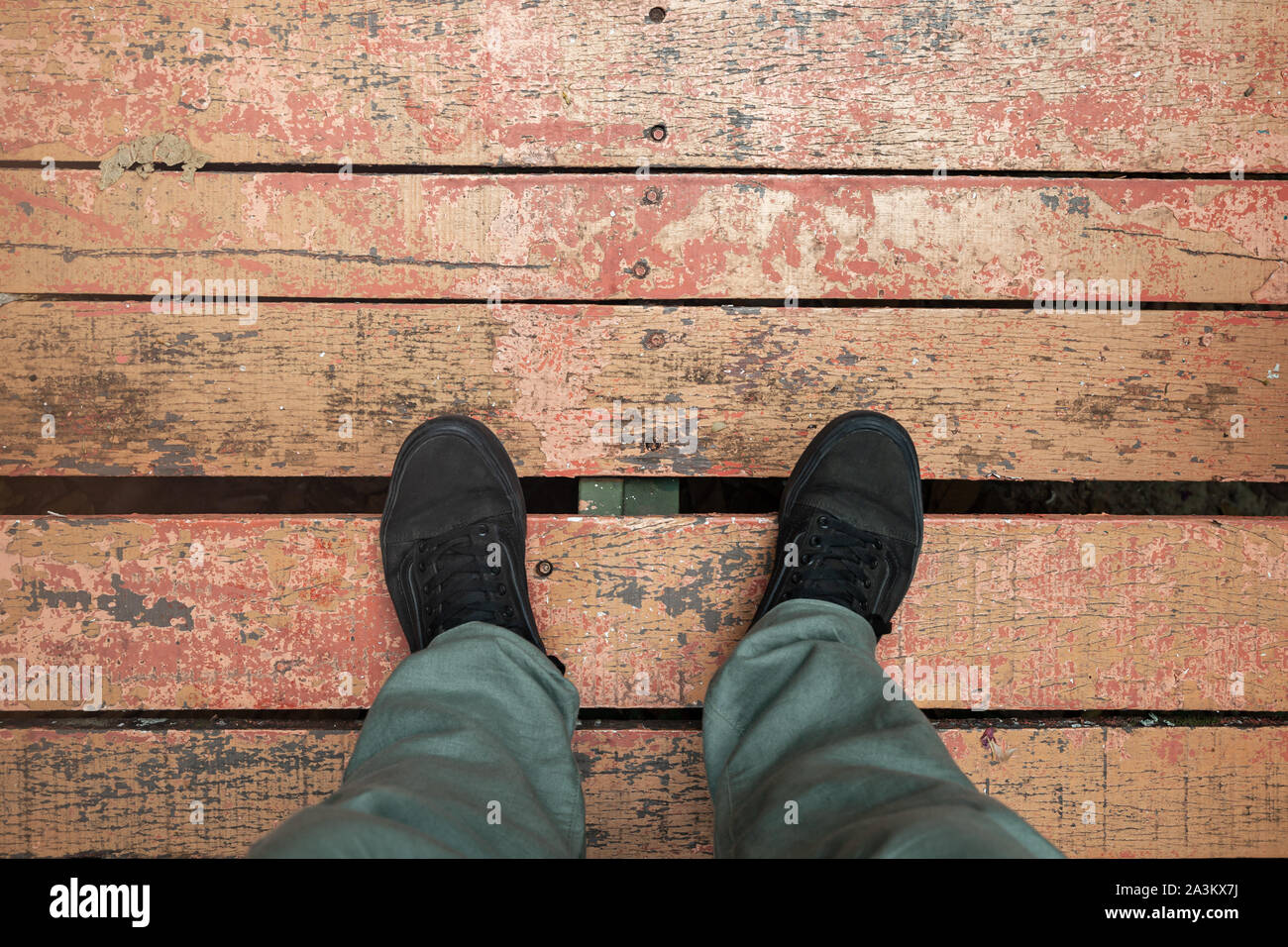 Männliche Füße in schwarzen Sneakers stehen auf Grunge red Holzboden, erste Person anzeigen Stockfoto