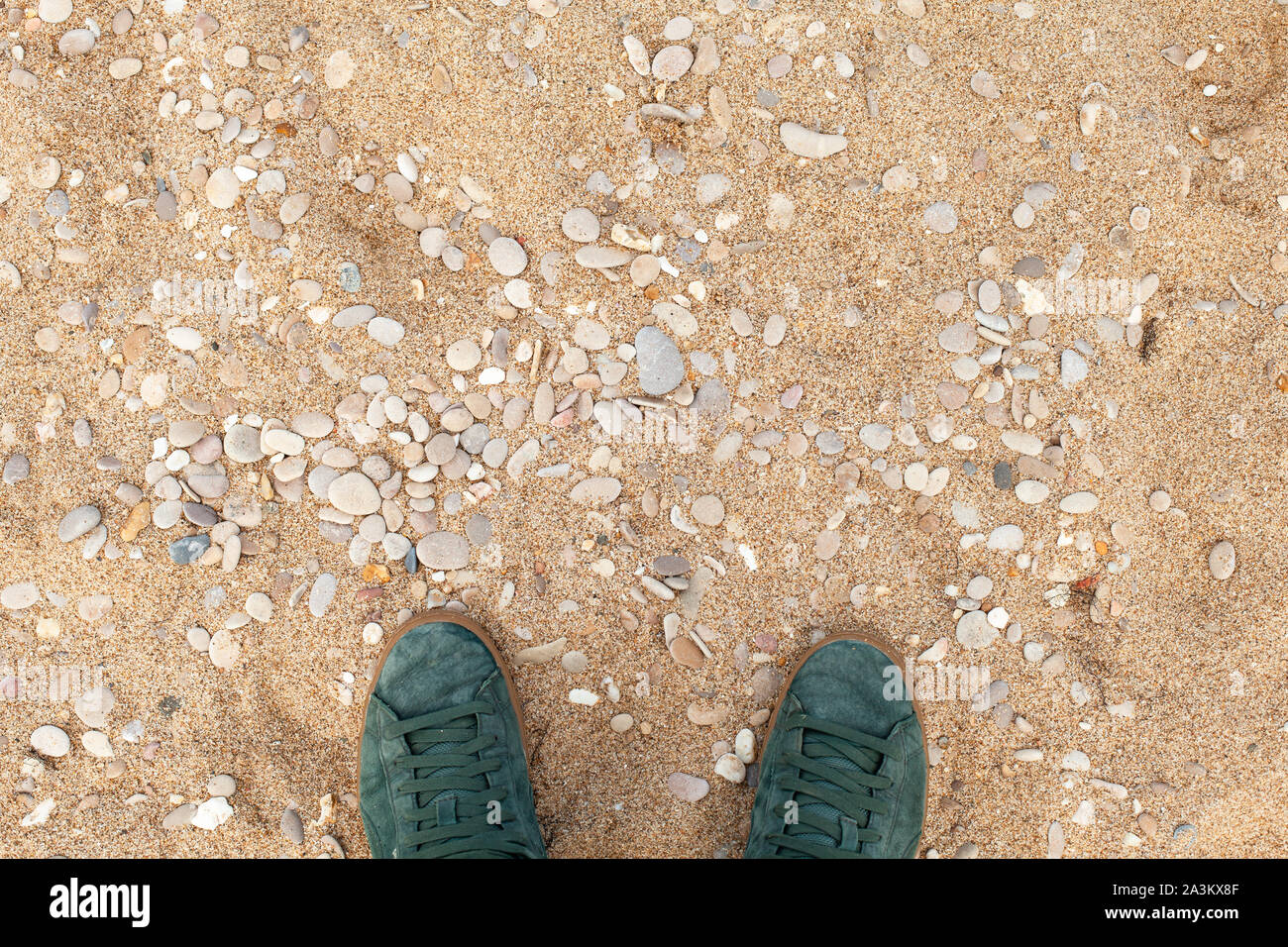 Männliche Füße in Grün sportlich Wildleder Schuhe stehen auf sandigen Strand mit Kiesel, erste Person anzeigen Stockfoto