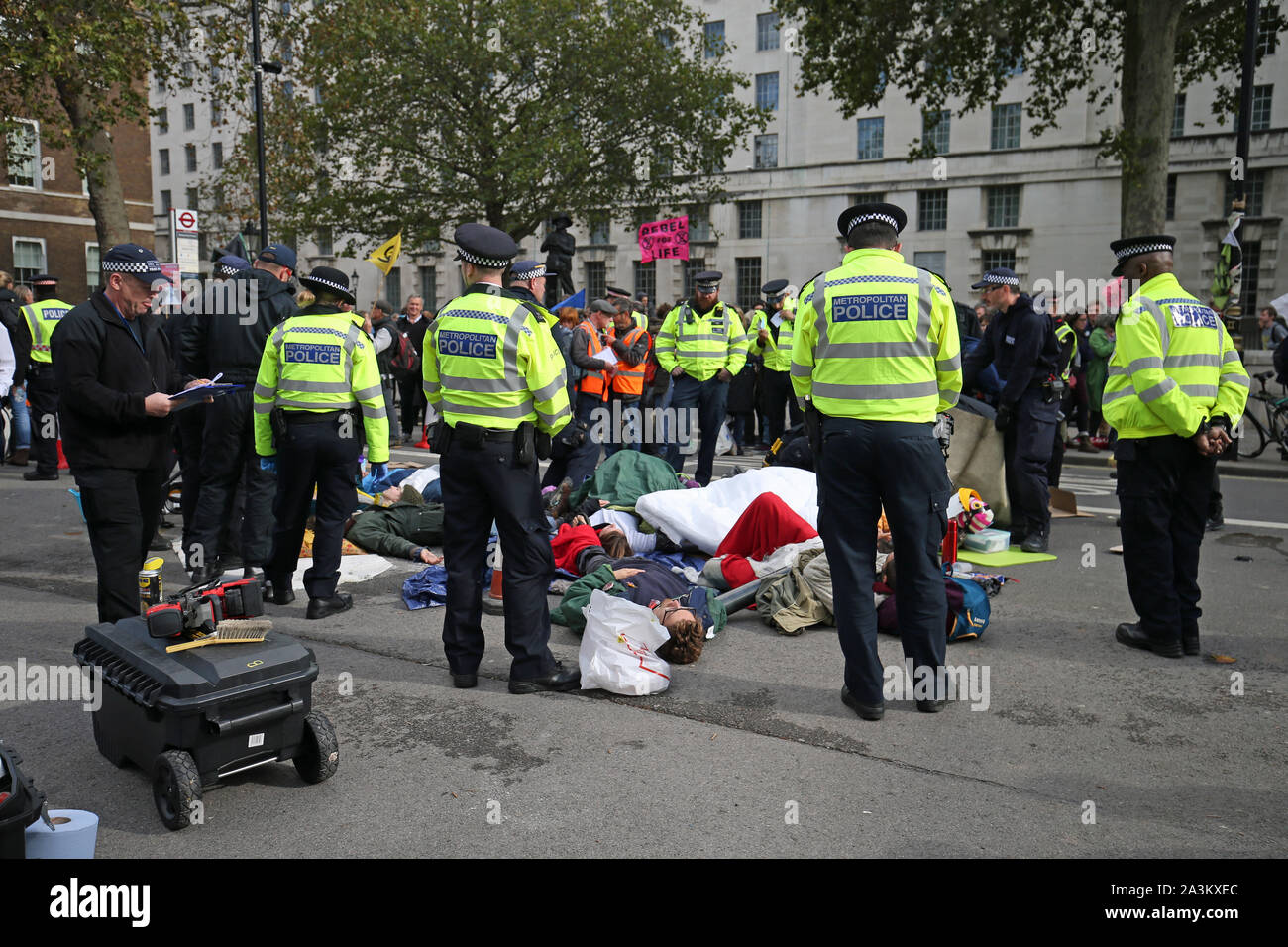 Polizei Form ein Cordon rund um die Demonstranten, die sich gegenseitig in einem Kreis geklebt haben, neben den Frauen im Zweiten Weltkrieg Gedenkstätte auf Whitehall, während der dritte Tag der Auslöschung Rebellion (XR) Protest in Westminster, London. Stockfoto