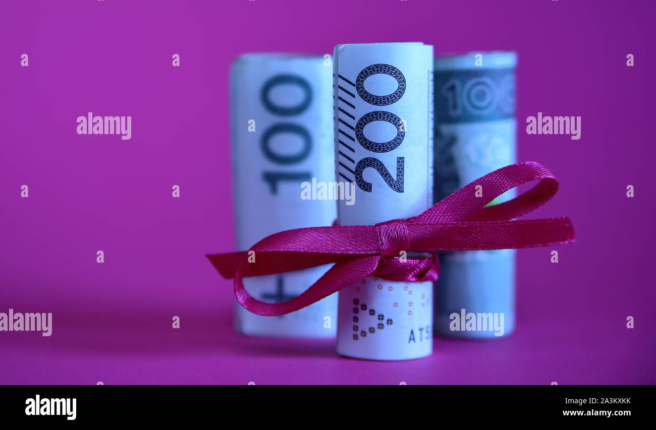 Banknoten, die von 200 polnischen Zloty rollte in Rollen und mit roter Schleife gebunden, hinter zwei Rollen von 100 Zloty, Konzept der finacial Geschenk, lila Hintergrund Stockfoto