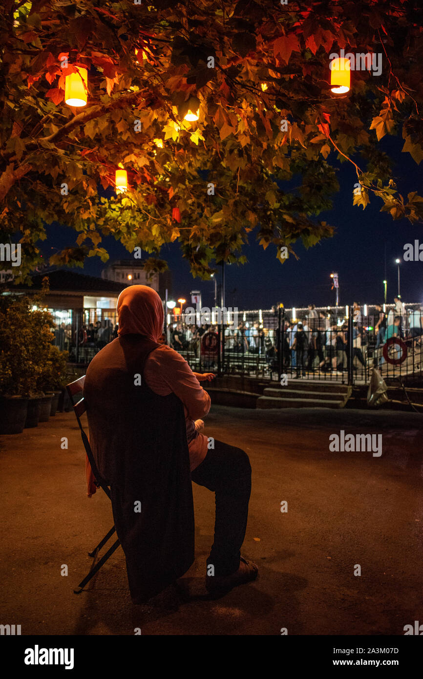 Istanbul: das Nachtleben in der Stadt, eine türkische Frau auf einem Stuhl unter einem Baum mit bunten Laternen dekoriert sitzt und umschließen ein Baby in den Straßen Stockfoto