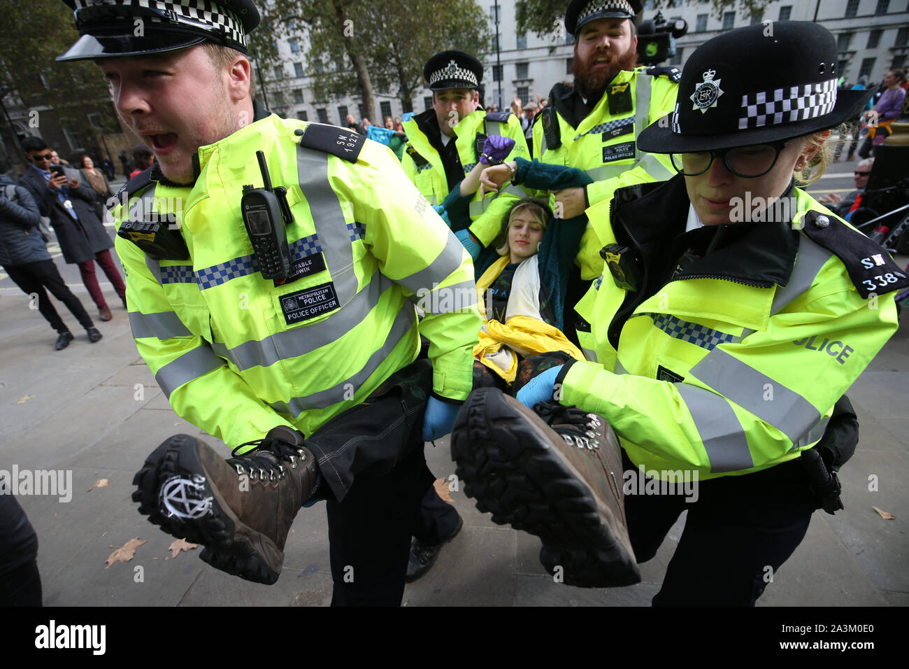 Polizei nimmt eine Demonstrantin, die sich mit Anderen in einem Kreis geklebt worden war, neben den Frauen im Zweiten Weltkrieg Gedenkstätte auf Whitehall, während der dritte Tag der Auslöschung Rebellion (XR) Protest in Westminster, London. Stockfoto