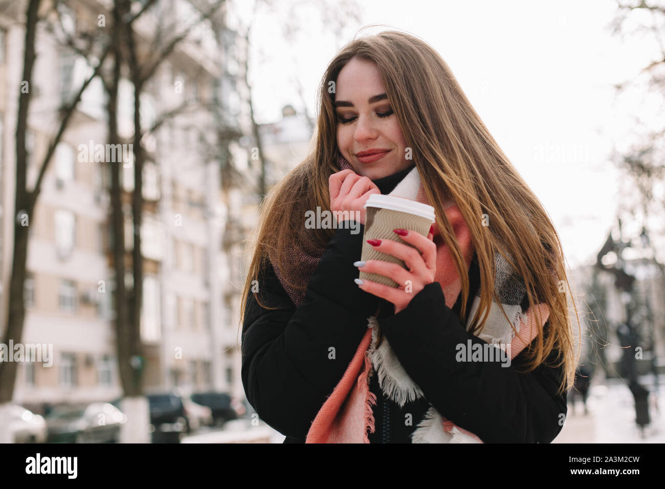 Glückliche junge Frau mit Einweg Becher warme Kleidung tragen, beim Gehen auf der Straße im Winter Stockfoto