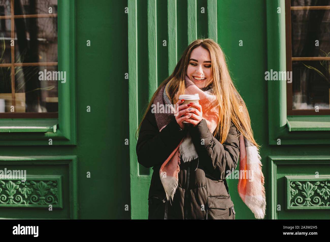 Glückliche Frau mit Schale in warme Kleidung stand neben Green Building in Stadt Straße im Winter Stockfoto