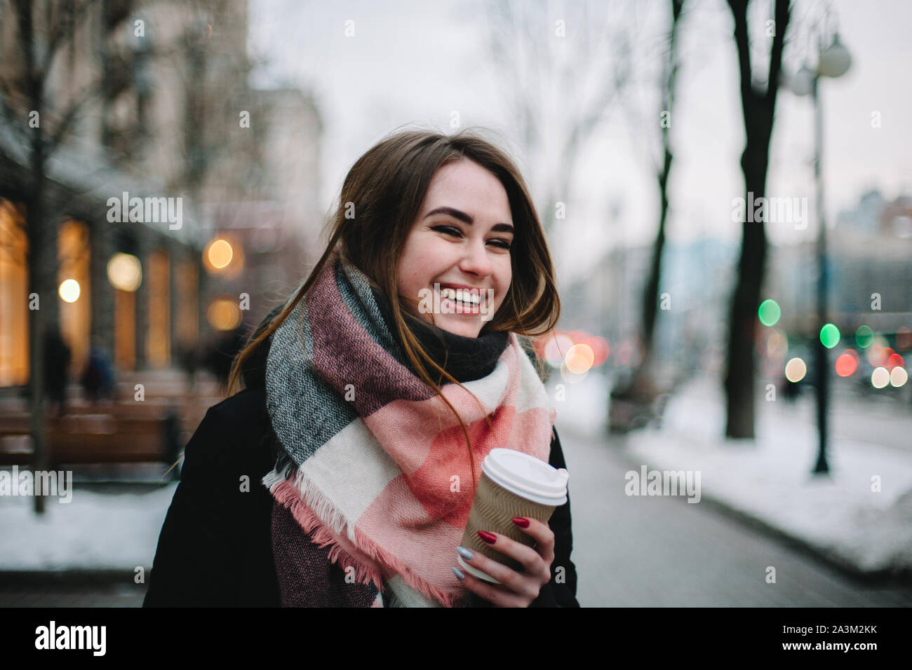 Glückliche junge Frau mit Einweg Becher warme Kleidung tragen, beim Gehen auf der Straße im Winter Stockfoto