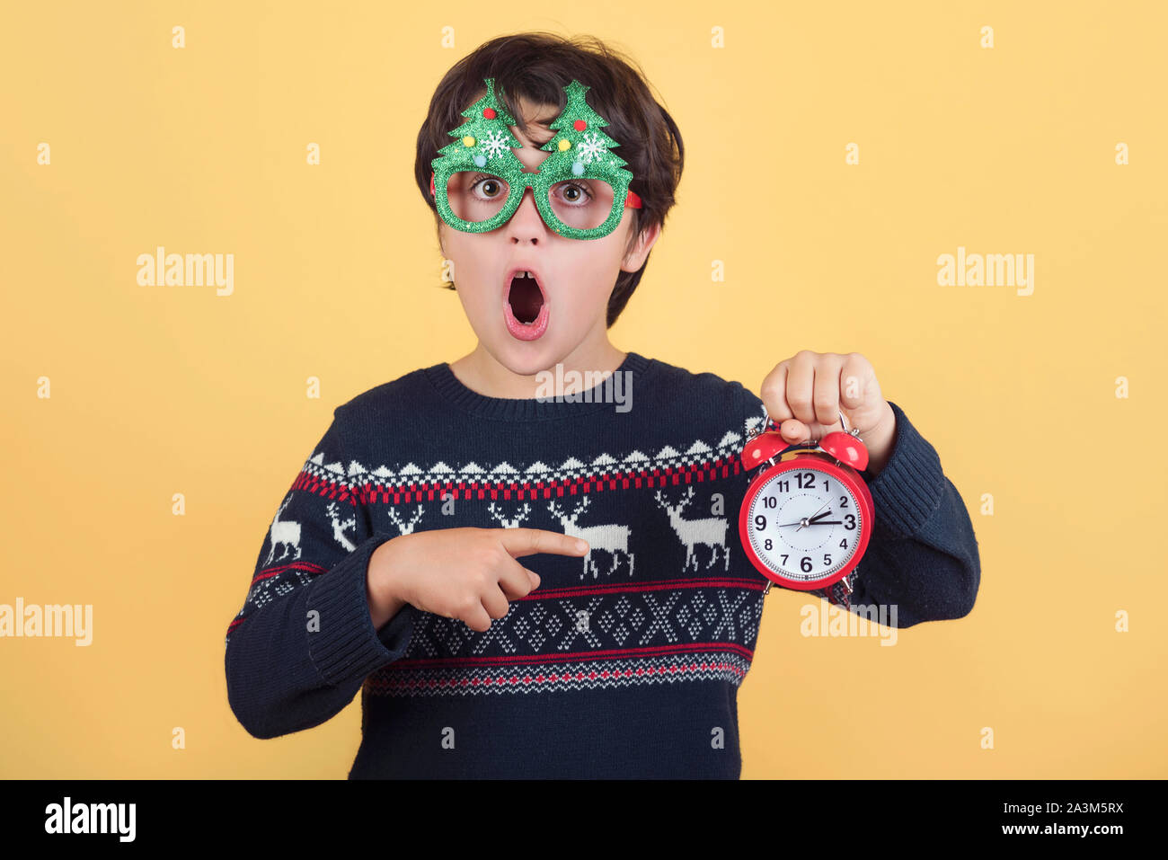 Überrascht Kind mit Wecker Tragen lustig Weihnachten Brille auf gelbem Hintergrund Stockfoto