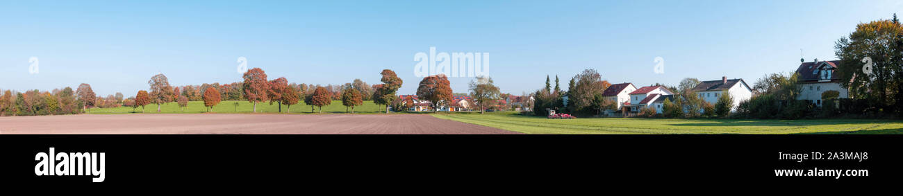Ländliche Landschaft, Panoramablick auf ein kleines Dorf, mit einem Traktor workingin ein Feld, ein paar Häuser und viele Bäume mit Laub im Herbst gelb. Bayerische c Stockfoto
