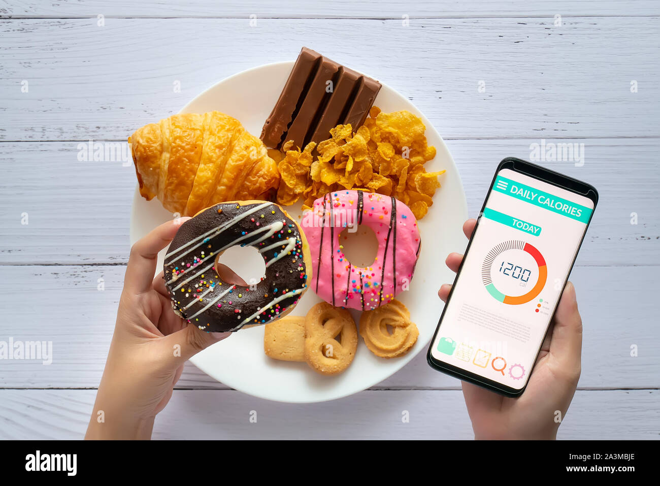 Kalorien zählen und die Lebensmittelüberwachung Konzept. mit Kalorienzähler Anwendung auf Ihrem Smartphone mit Donut in der Hand und Snack Frau, Cookies auf Pla Stockfoto
