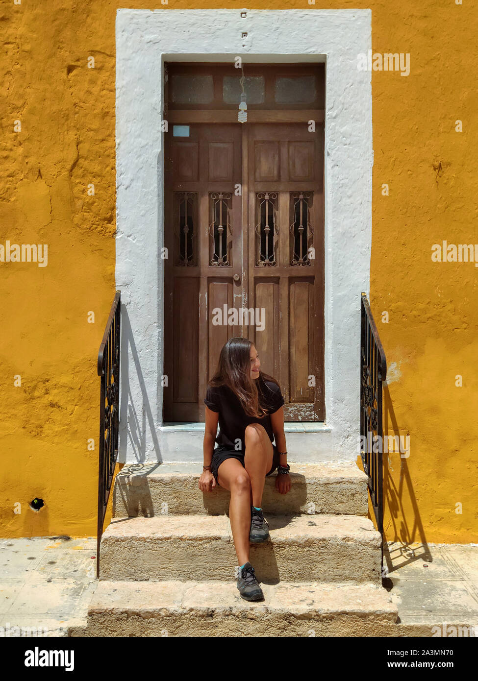 Frau sitzt in einem typischen kolonialen Fassade in Gelb mit Holztür, Izamal (Mexiko) Stockfoto