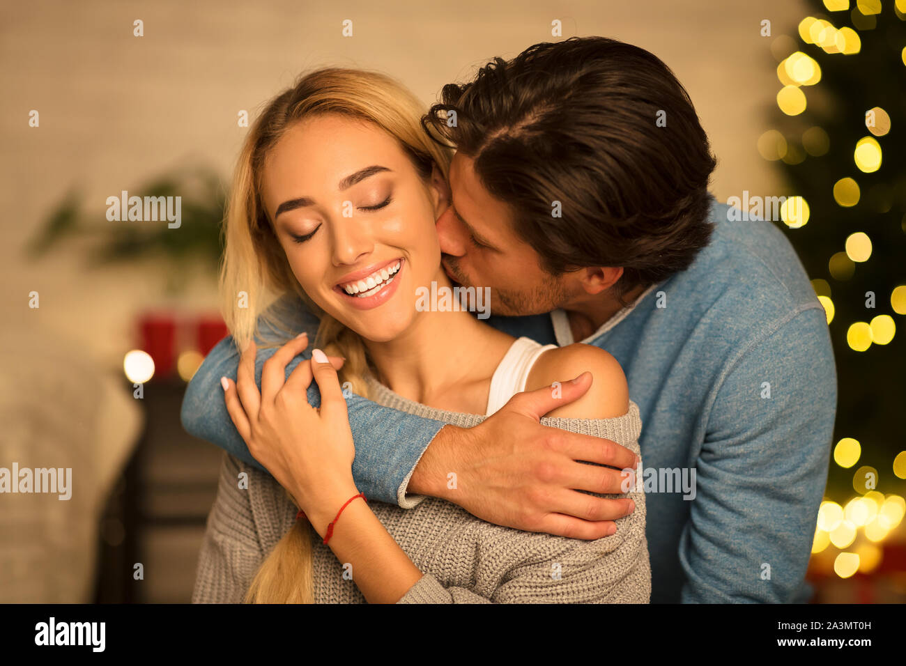 Mann küssen Hals von atemberaubenden Frau sitzt in der Nähe von Weihnachten Baum Stockfoto