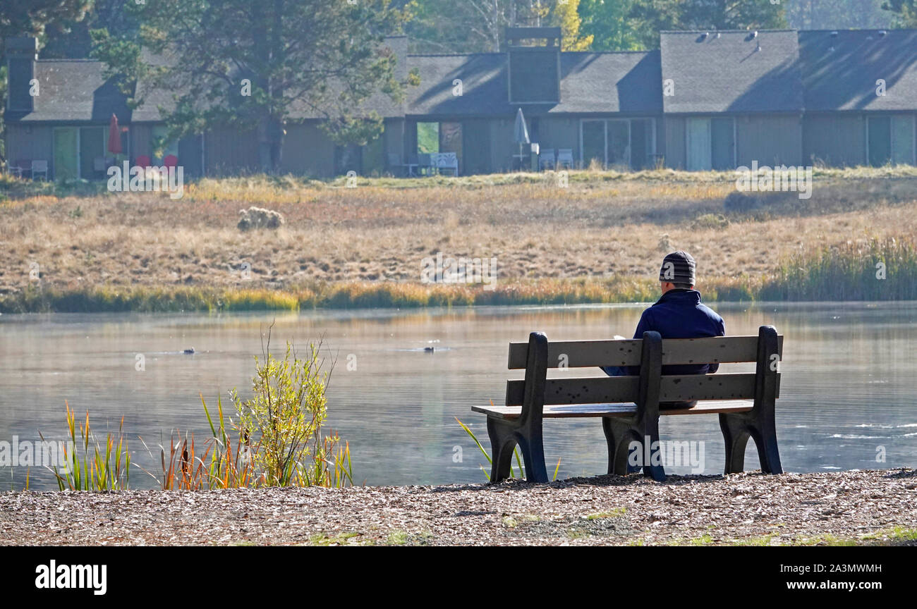 Ein Mann sitzt auf einer ruhigen Bank entlang einer Misty River am frühen Morgen, das Lesen einer Zeitschrift, in der zentralen Oregon. Stockfoto