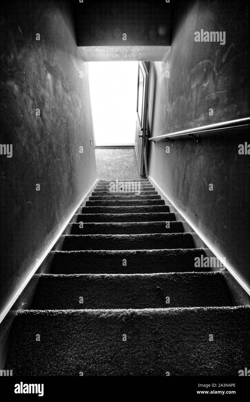 Vertikale abgeschossen, die eine dunkle treppe, um die Leuchte aus eine offene Tür an der Unterseite. Schwarz-weiss Bild. Stockfoto