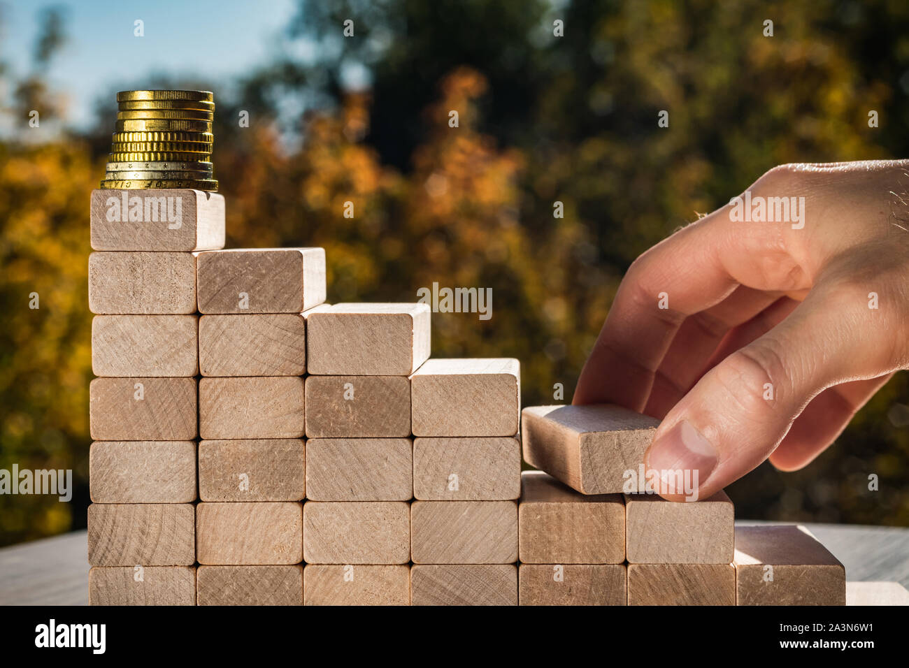Konzept der Wirtschaftsförderung Ziele. Männliche Finger bauen Treppen aus Holz- Bausteine, die zu den Top. Blurry Herbst Hintergrund an einem sonnigen Tag. Stockfoto