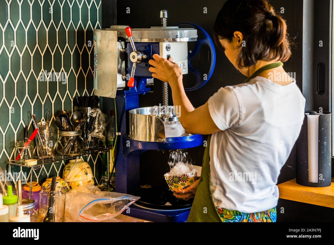 Ein Angestellter dreht das Rad der Kakigori-Maschine, feiner gehobeltes Eis fällt in eine farbenfroh gemusterte Schale. Café in Shizuoka, Präfektur Shizuoka, Japan. Stockfoto