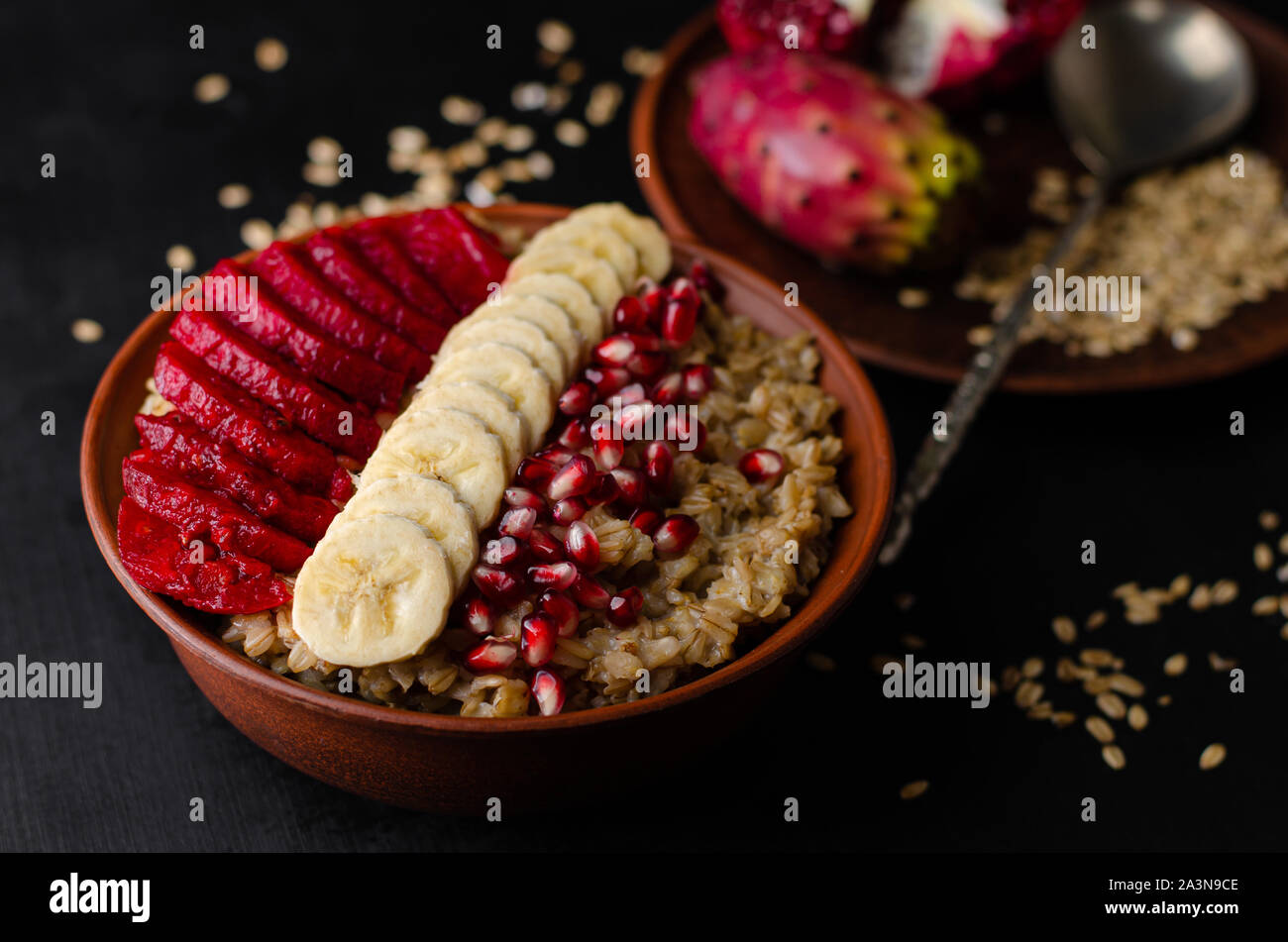 Nahaufnahme von einer Schüssel mit haferflockenbrei, Banane, Granatapfel Samen und Opuntia Kakteen Obst auf schwarzem Hintergrund. Stockfoto