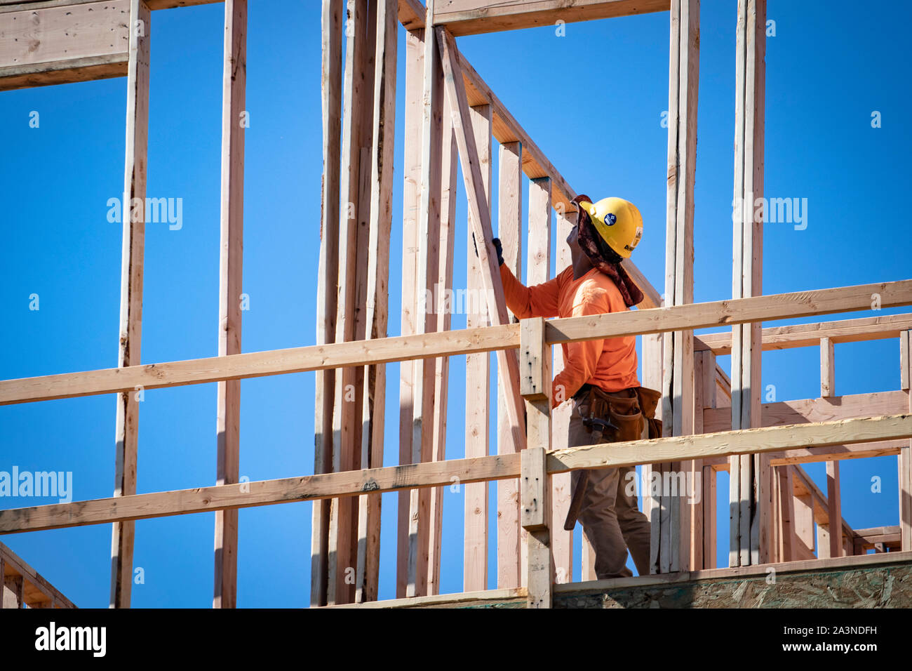 Bauarbeiter in Sicherheitsausrüstung umrahmen ein großes Wohnhaus an einem heißen sonnigen Tag. Stockfoto