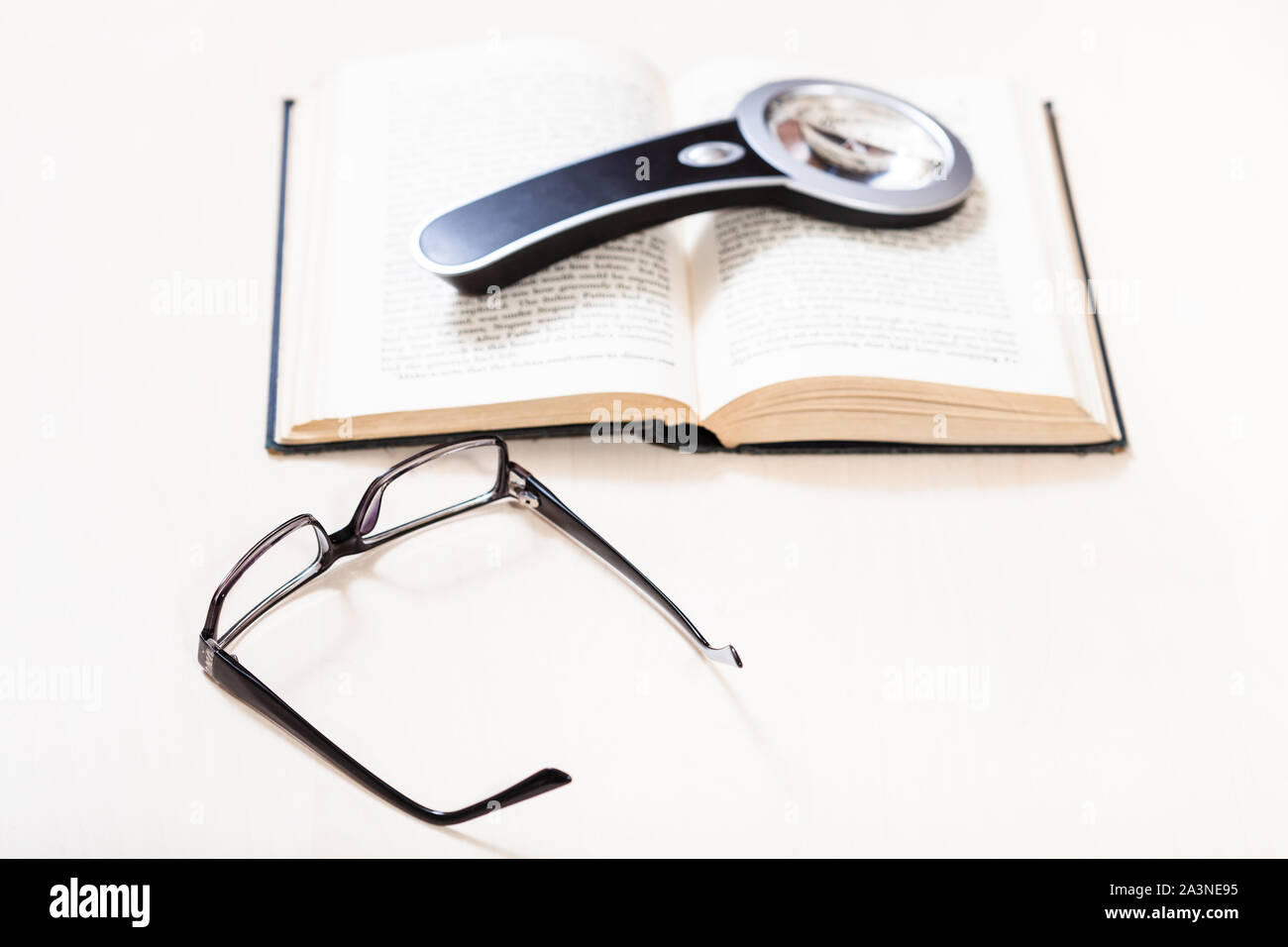 Lesen Buch mit Low Vision - Brille und Lupe auf offenen Buch über blasse Tabelle (Schwerpunkt im Vordergrund) Stockfoto