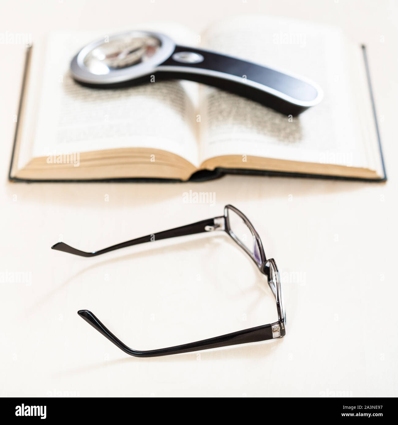 Lesen Buch mit Low Vision-Brille und Lupe auf offenen Buch über blasse Tabelle (Schwerpunkt im Vordergrund) Stockfoto
