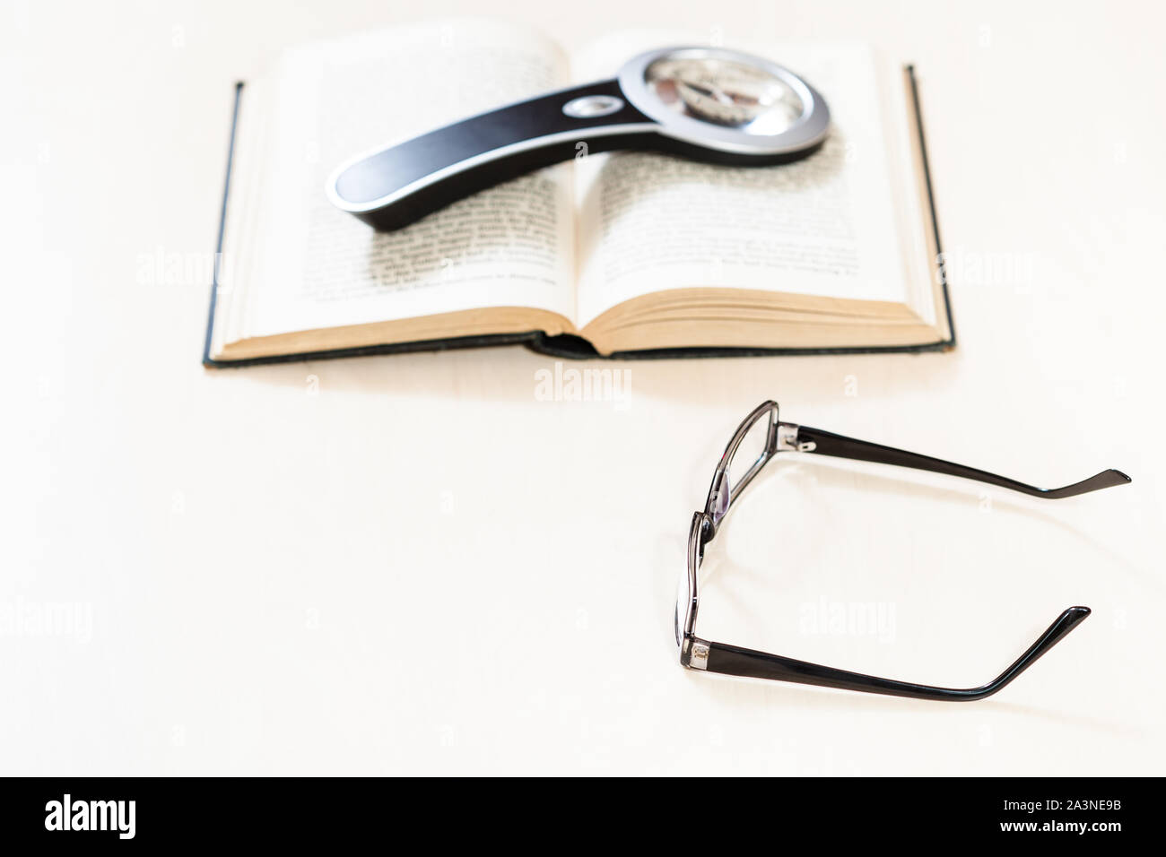 Lesen Buch mit Low Vision-Brille und Lupe auf offenen Buch über blasse Tabelle (Schwerpunkt im Vordergrund) Stockfoto