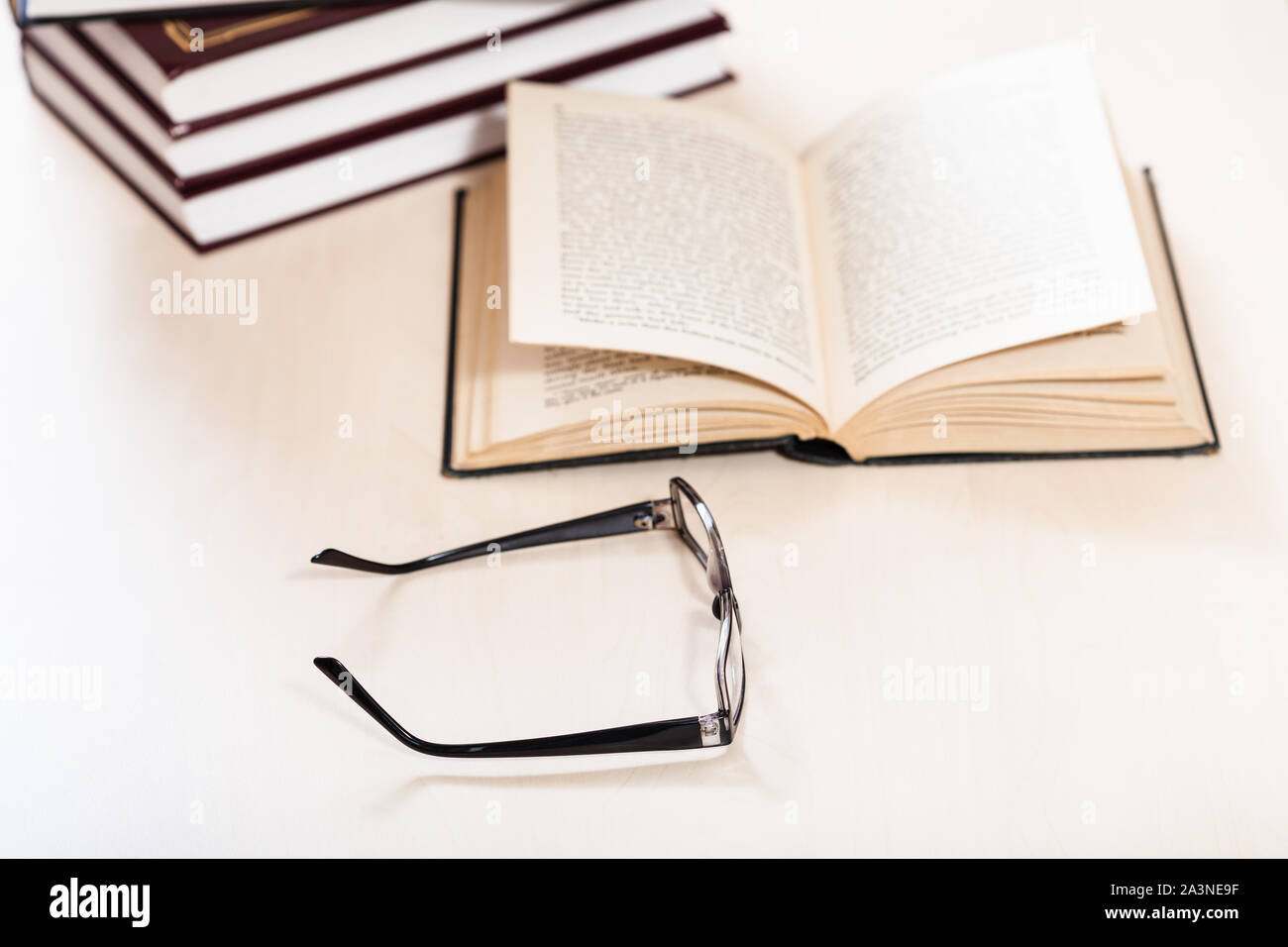 Lesen Buch mit Low Vision - Brillen und offenen Buch in der Nähe der Bücher auf dem blassen Tabelle stack (Schwerpunkt im Vordergrund) Stockfoto